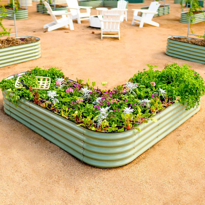 Sage V-shaped corrugated raised garden bed filled with herbs, vegetables, and flowers. Outdoor patio with white Adirondack chairs.