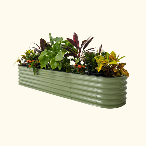 Long sage green corrugated metal raised garden bed filled with vibrant green, red, and yellow plants, plus flowers.