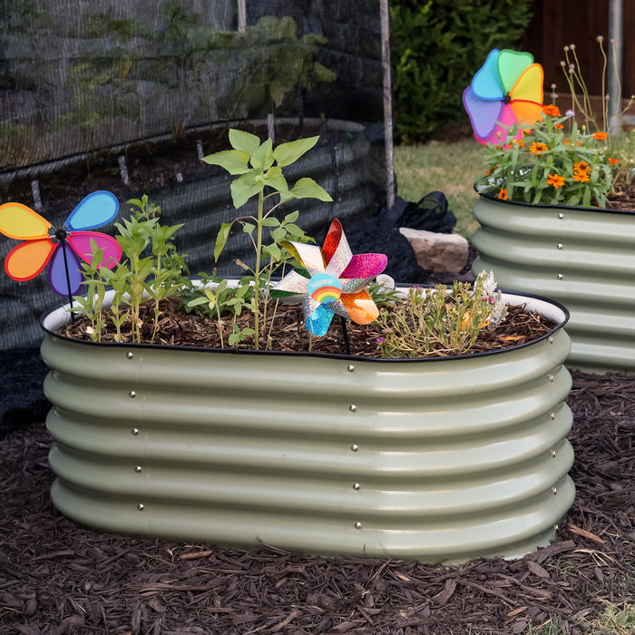 Backyard with two sage green corrugated steel raised garden beds, vibrant plants, orange flowers, and colorful pinwheels.