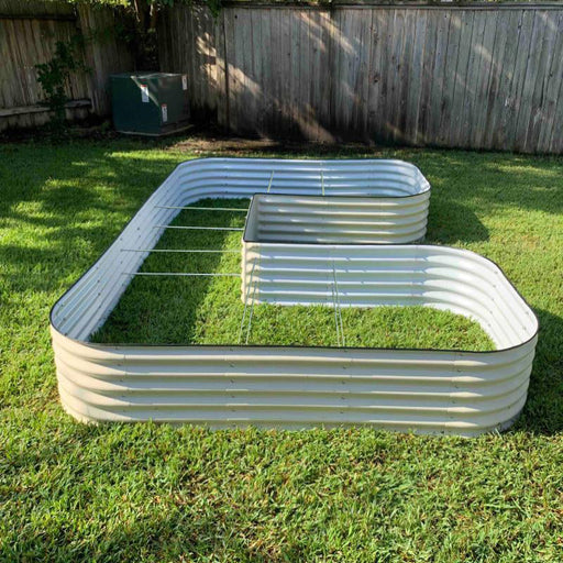Beige corrugated steel L-shaped raised garden bed on green grass. Outdoor backyard planter.