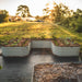L-shaped corrugated steel raised garden beds growing vegetables with mulch, weed fabric, and greenhouses at sunset.