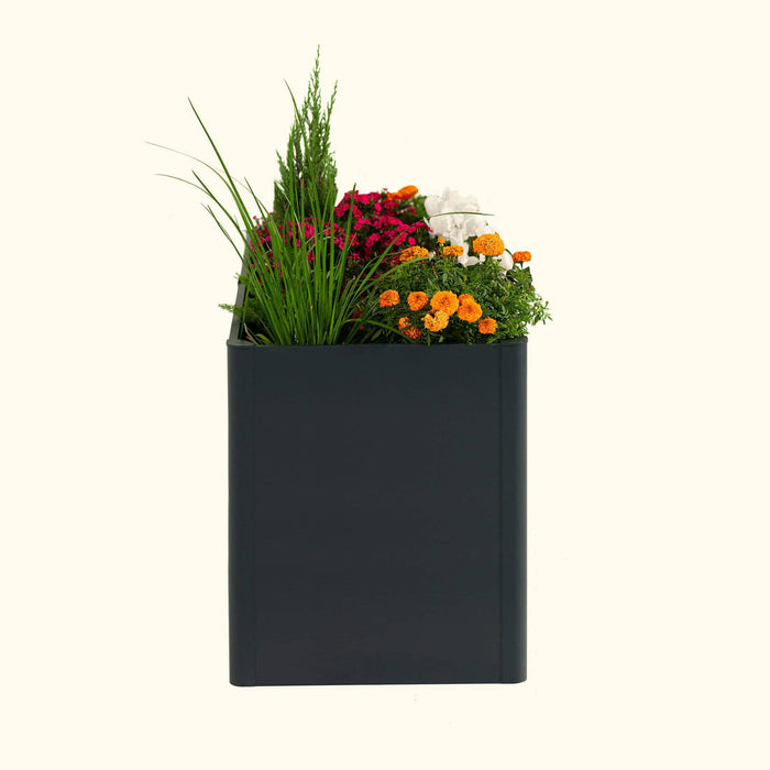 Modern dark grey rectangular planter box filled with vibrant pink, orange, and white flowers, green grass, and evergreen.