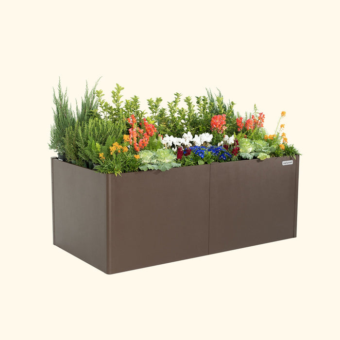 Brown Vego Garden metal raised planter box with vibrant flowers, lush green plants, and evergreens.