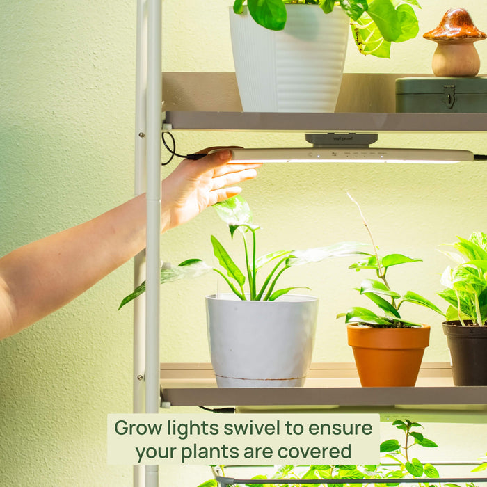 Hand adjusting Vego Garden LED grow light on a plant shelf, illuminating diverse indoor plants. Swivel design ensures full coverage for plant growth.