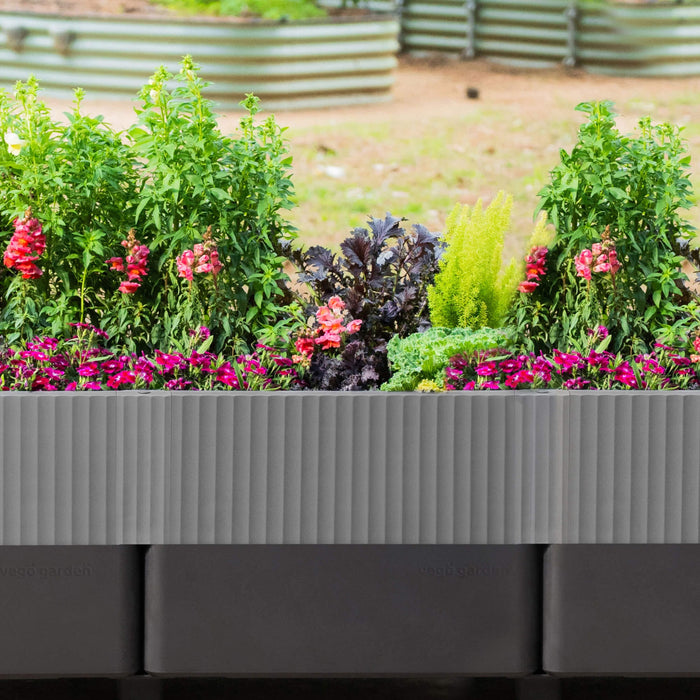 Ribbed gray modular raised garden bed by Vego Garden, brimming with pink snapdragons, fuchsia dianthus, and diverse greens.