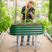 Woman tends young plants in a green Vega Garden mobile raised garden bed on wheels. Ideal for small space gardening.