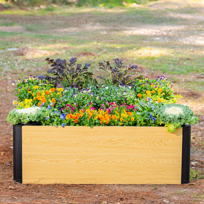 Wood grain raised garden bed with black frame, filled with vibrant pansies, orange flowers, and ornamental kale.