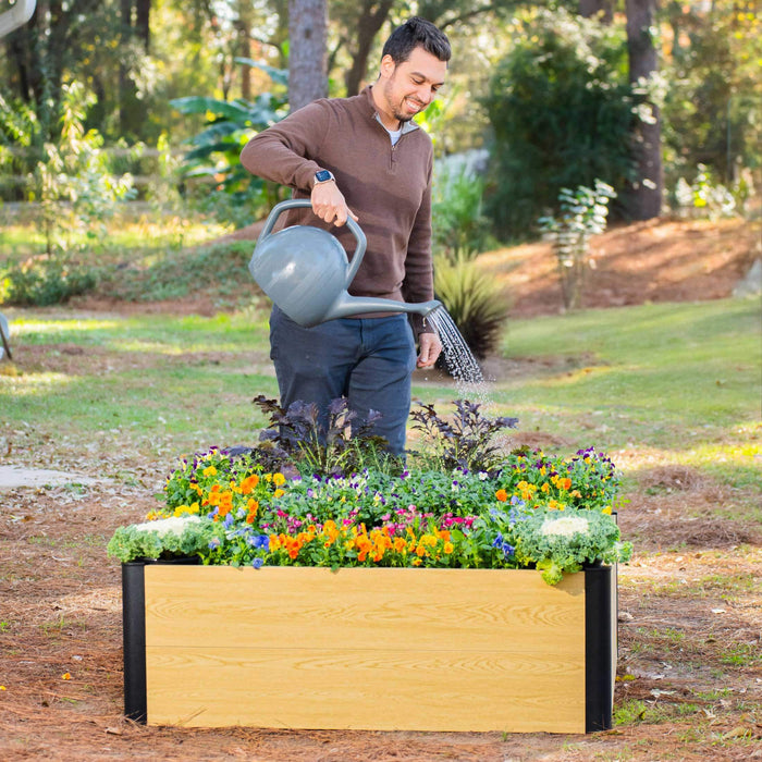 Happy man watering vibrant flowers and plants in a modern wood-look raised garden bed. Perfect for home gardening.