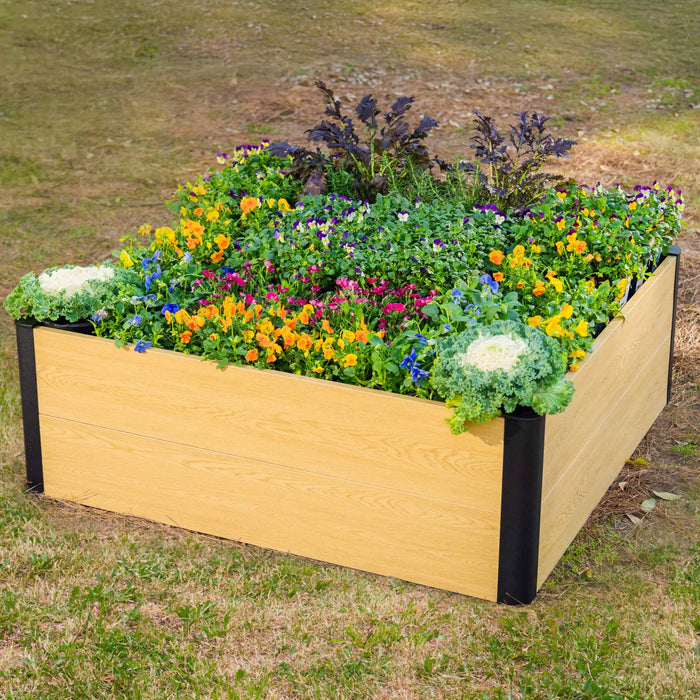 Light wood-grain composite raised garden bed with black corners, filled with colorful flowers, pansies, and kale.