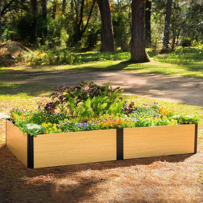 Light wood-look raised garden bed with black posts, brimming with colorful flowers, kale, and ferns in an outdoor landscape.