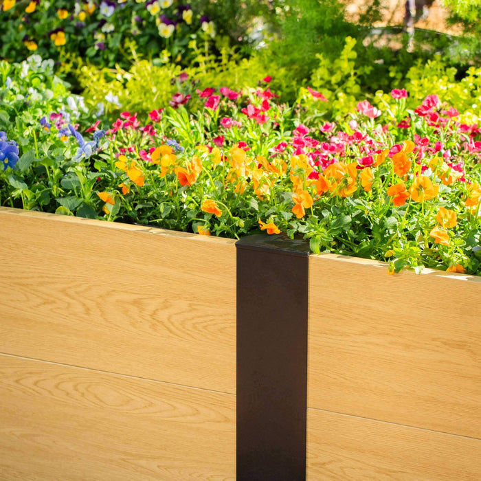Modern light wood planter box with a dark metal accent, filled with vibrant blue, orange, and pink garden flowers.