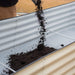 Filling a two-tone corrugated steel raised garden bed with dark soil for backyard gardening and planting.