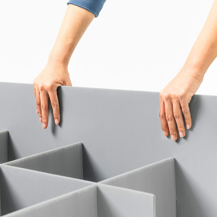 Hands place grey corrugated plastic divider into a modular multi-compartment storage organizer.