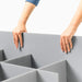 Hands place grey corrugated plastic divider into a modular multi-compartment storage organizer.
