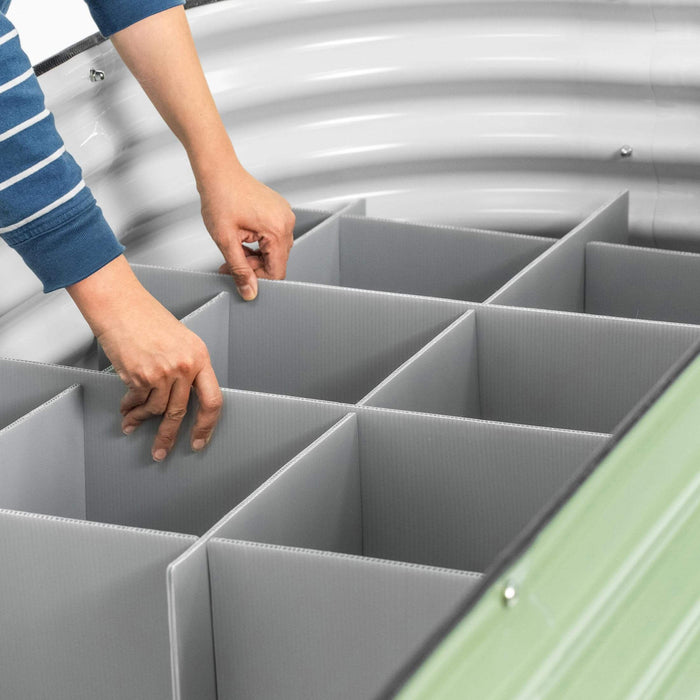 Person installing gray dividers inside a round, green corrugated metal raised garden bed for soil separation.