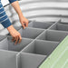 Person installing gray dividers inside a round, green corrugated metal raised garden bed for soil separation.