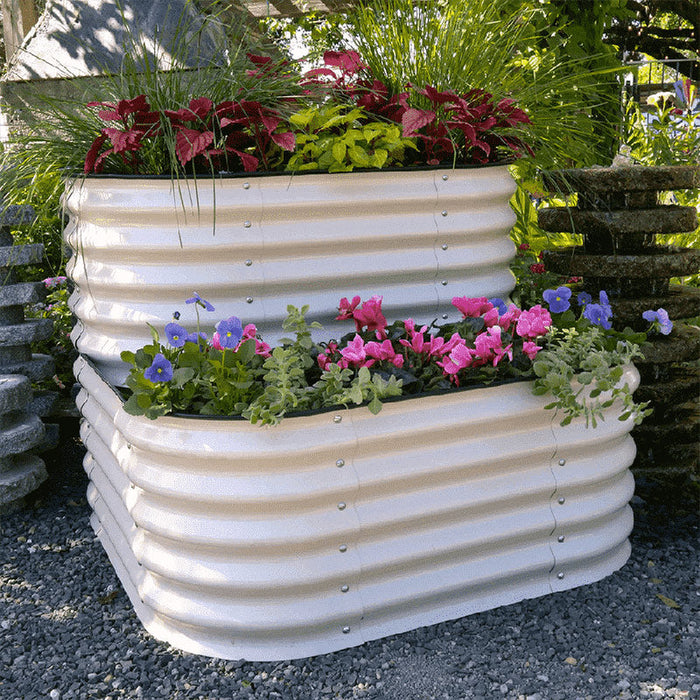 Cream corrugated metal corner raised garden beds with vibrant pink, blue, red flowers and lush green plants.