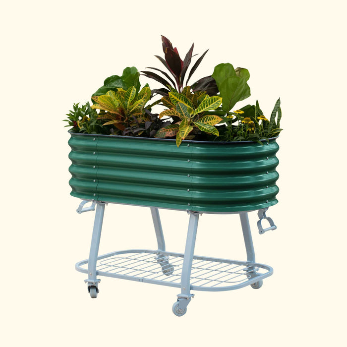 Green corrugated metal mobile raised garden bed on wheels, filled with colorful plants and a storage shelf.