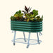 Green corrugated metal mobile raised garden bed on wheels, filled with colorful plants and a storage shelf.