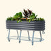 Dark grey corrugated metal raised garden bed on wheels, filled with diverse plants, featuring a lower storage shelf.