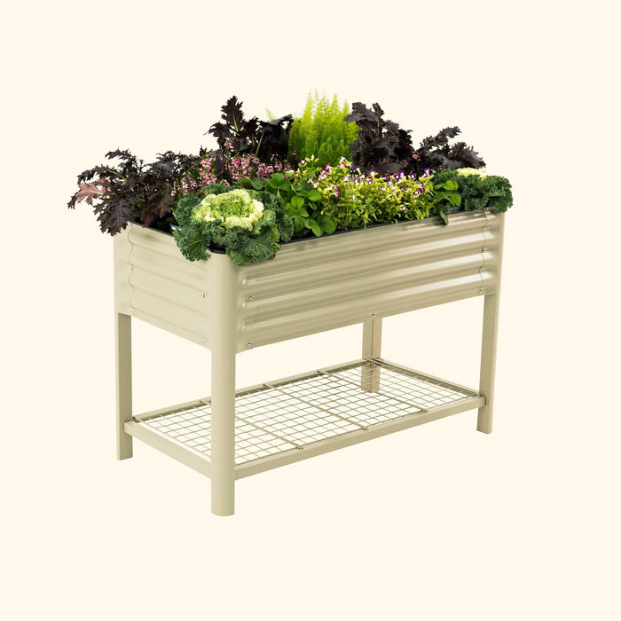 Beige corrugated metal raised garden bed with various colorful plants, flowers, and greens. Features a lower storage shelf.