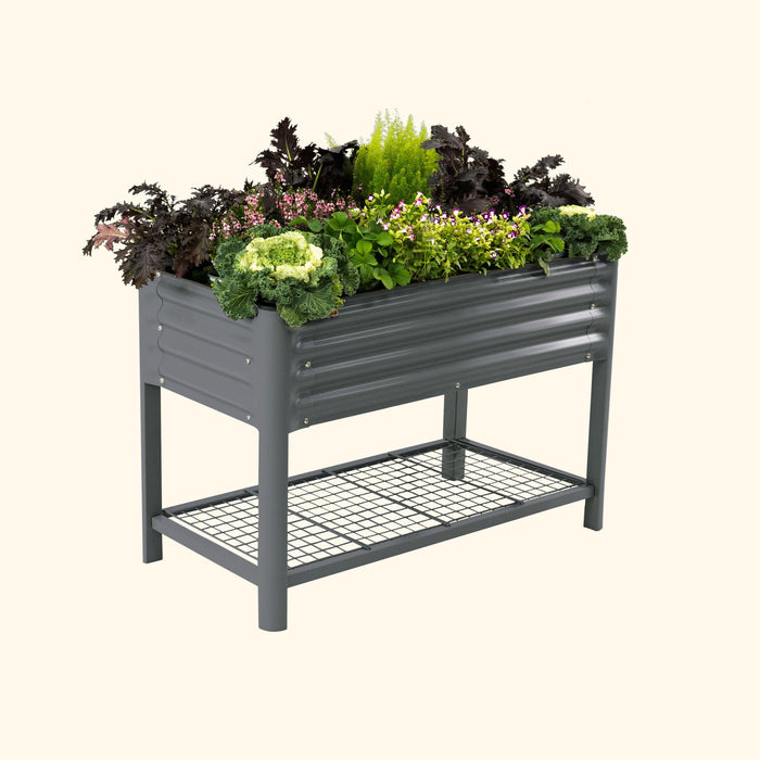 Dark gray corrugated metal raised garden bed, filled with green plants and colorful flowers, includes a lower wire storage shelf.