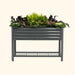 Charcoal corrugated metal raised garden bed with kale, greens, ferns, and pink flowers. Elevated planter with storage shelf.