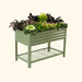 Sage green corrugated metal raised garden bed with lower shelf, brimming with kale, red mustard, and colorful flowers.