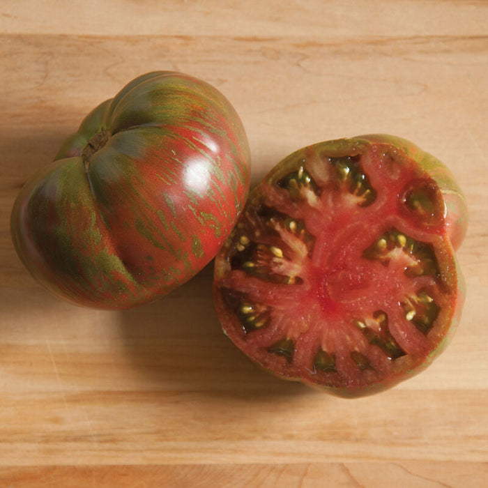 Vibrant red and green striped heirloom tomato, whole and sliced, displaying juicy flesh and seeds on a wooden board.