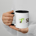 White mug with black handle, green seedling logo, and "SE" text, held by hands.