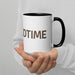 White ceramic mug with black handle and interior, featuring brown "DTIME" text, held by hands in a white sweater.