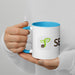 Hand holding white mug with blue rim & handle. Features green sprout logo and SEED text. Perfect for beverages.