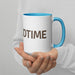 Hands holding a white ceramic mug with blue rim and handle. Brown "DTIME" text printed on the side.