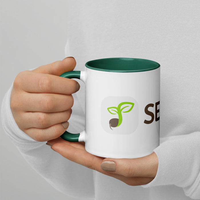 White mug with green rim, held by hands. Features a green seed sprout logo and 'SE' branding.