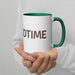 Person holding a white ceramic coffee mug with a green rim and handle, featuring partial text "DTIME". Custom drinkware gift.