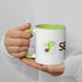 White coffee mug with a green handle and interior, featuring a sprouting seed logo and "SEED" text.