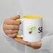 White mug with yellow handle, green seed sprout logo, and 'SE' text, held by hands. Branded coffee cup.