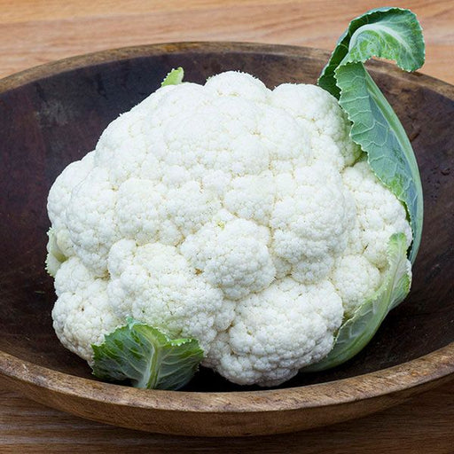 Fresh white cauliflower with green leaves in a rustic wooden bowl. Healthy whole vegetable.