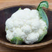 Fresh white cauliflower with green leaves in a rustic wooden bowl. Healthy whole vegetable.
