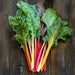 Fresh rainbow Swiss chard bunch with vibrant green leaves and colorful red, yellow, orange stems on dark wood.