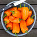 Bowl of fresh, vibrant orange mini bell peppers with a knife on a rustic wooden surface. Healthy cooking ingredients.