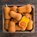 Harvested butternut squash in a wood crate, one sliced open showing vibrant orange flesh and seeds.