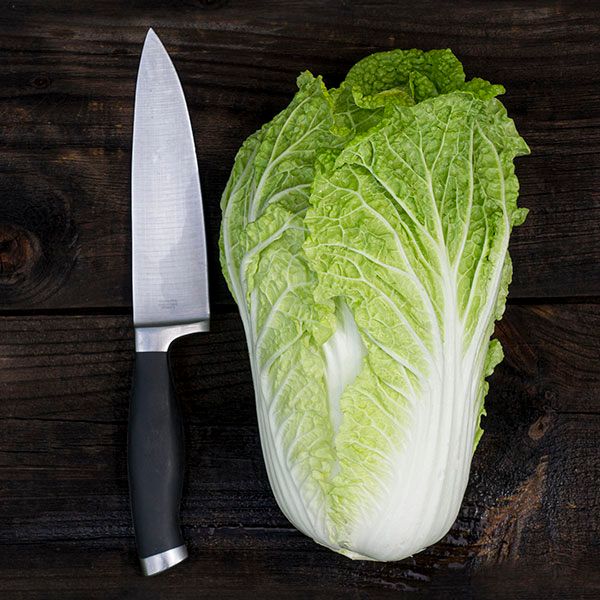 Fresh whole Napa cabbage and a chef's knife on a dark wooden surface.