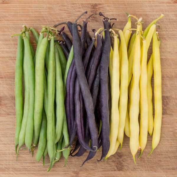 Fresh green, purple, and yellow wax bean varieties on a rustic wooden board.