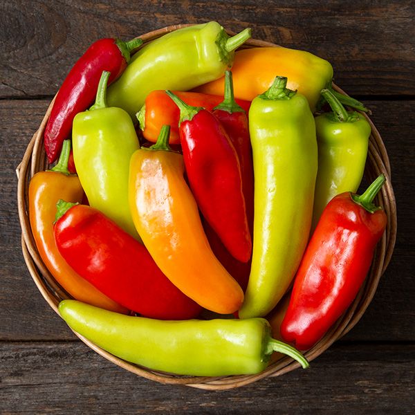 Basket of vibrant red, orange, yellow, and green sweet peppers on rustic wood.