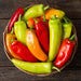 Basket of vibrant red, orange, yellow, and green sweet peppers on rustic wood.