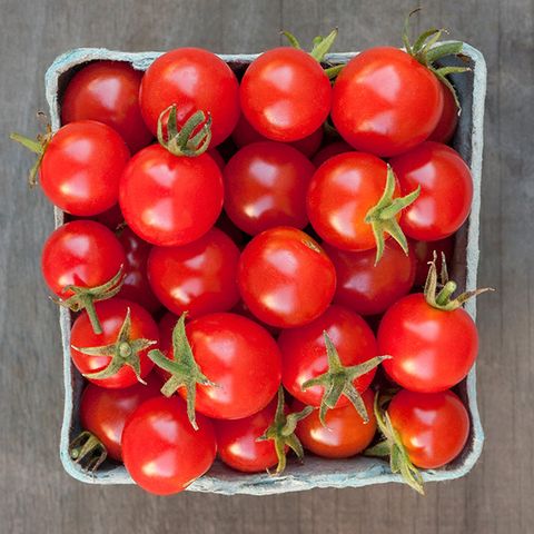 Fresh, ripe red cherry tomatoes with green stems in a light blue produce carton on wood.