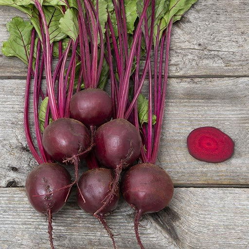 Fresh whole beets with green leaves and a vibrant sliced beet on rustic wood.