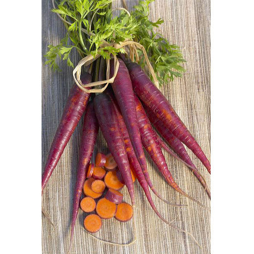 Fresh purple carrots with green tops, some sliced to reveal orange centers, on a natural woven mat.