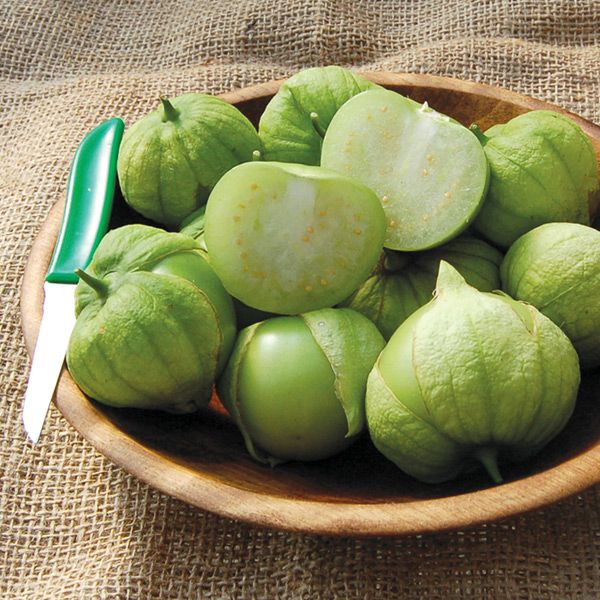 Fresh green tomatillos in a wooden bowl, one halved showing seeds. Perfect for salsa verde.